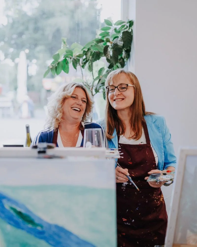 Zwei Teilnehmerinnen malen und lachen bei Entkorkte Kunst